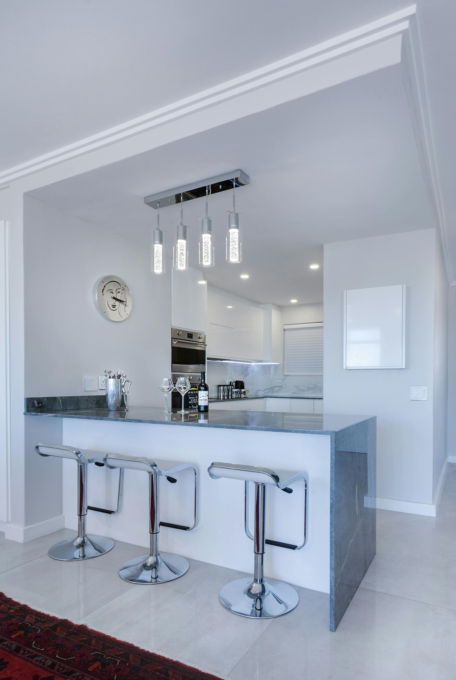 Kitchen with bar seating, white cabinets, and modern lighting.